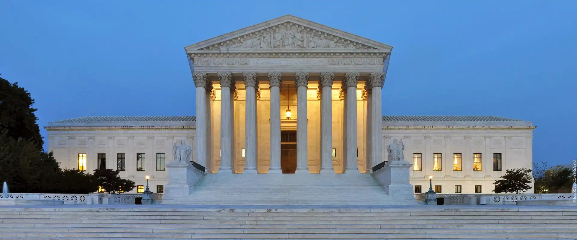 Neoclassical marble building with a grand entrance and illuminated windows.