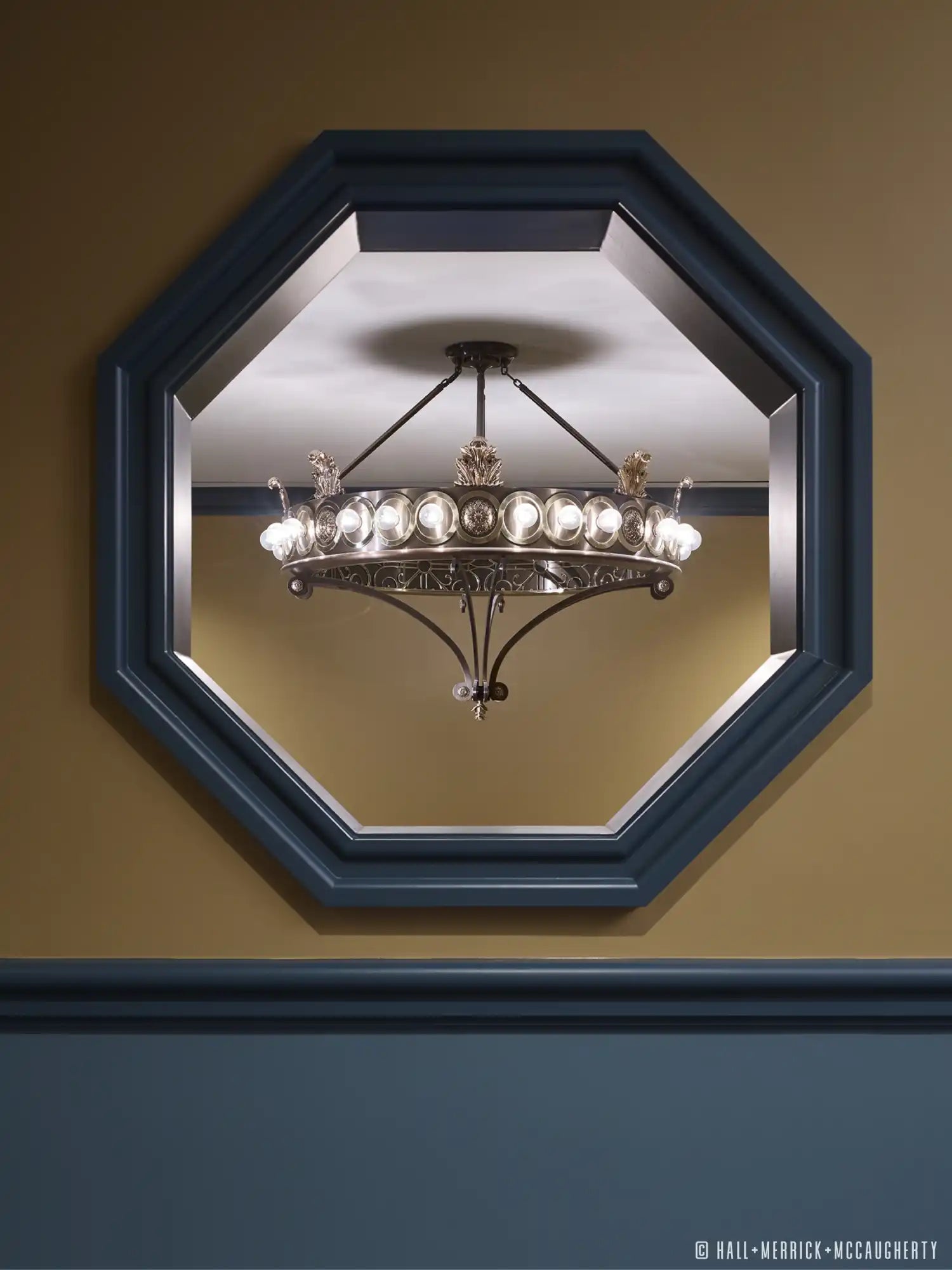 Ornate bronze chandelier with multiple glass bulbs, framed by an octagonal mirror.