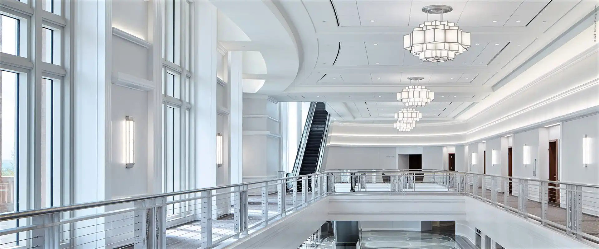 A well-lit, multi-level interior hallway with an escalator and modern chandeliers.