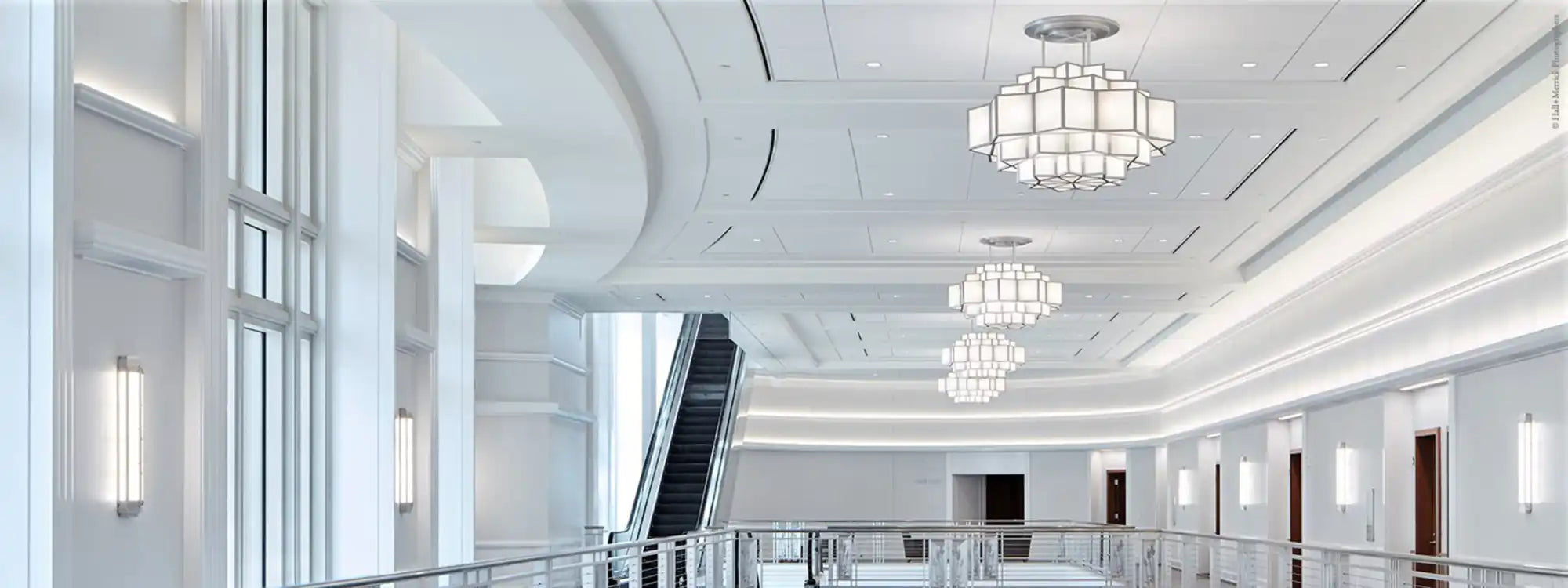 A modern, brightly lit interior hallway with an escalator and decorative chandeliers.