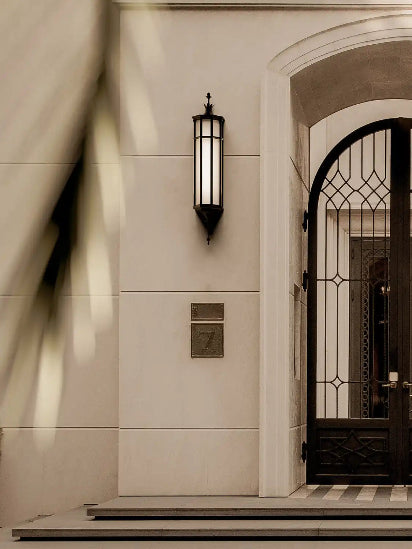 A tall, dark-framed outdoor wall lantern with an illuminated rectangular white glass panel.