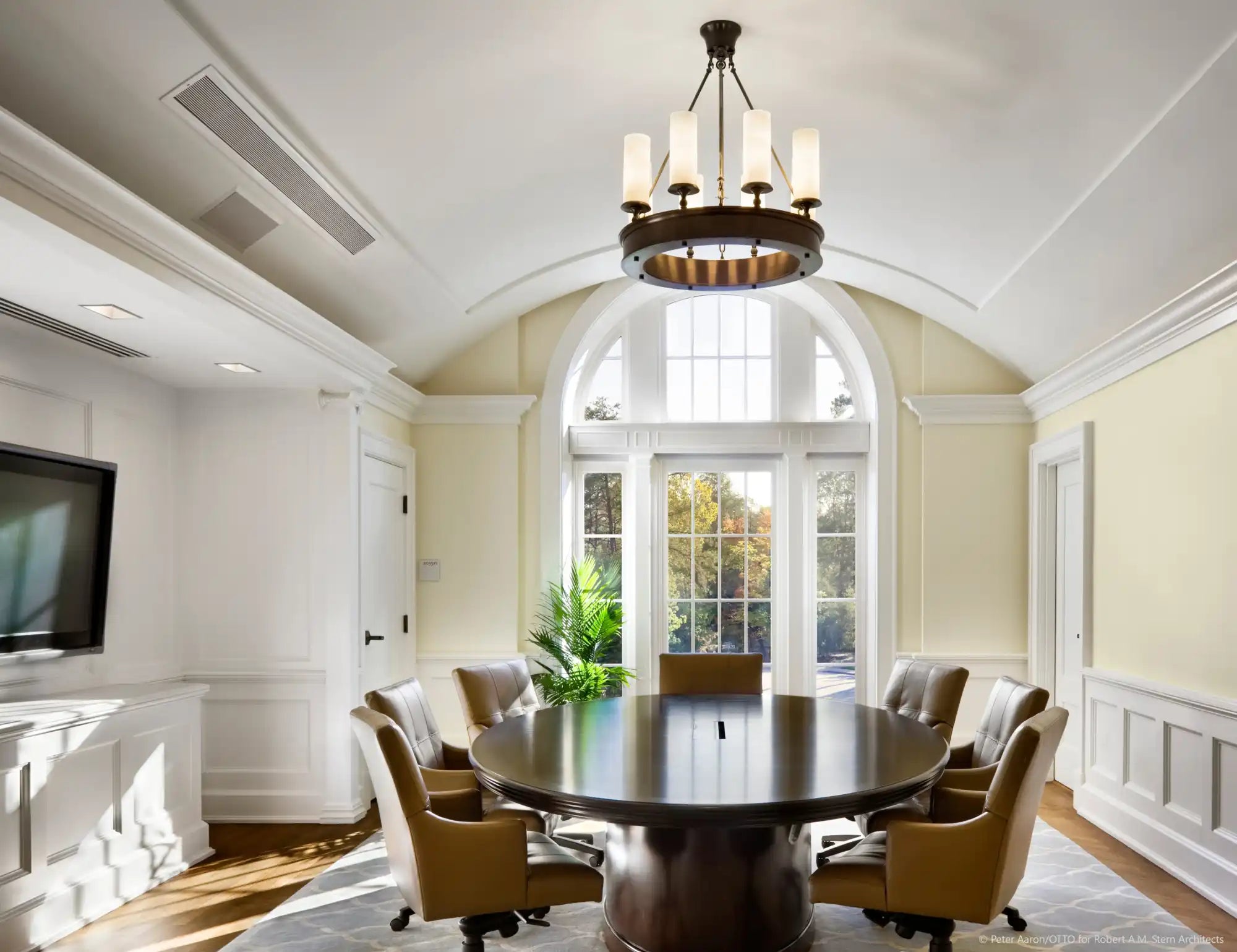 A round, dark wood conference table with eight brown leather swivel chairs.