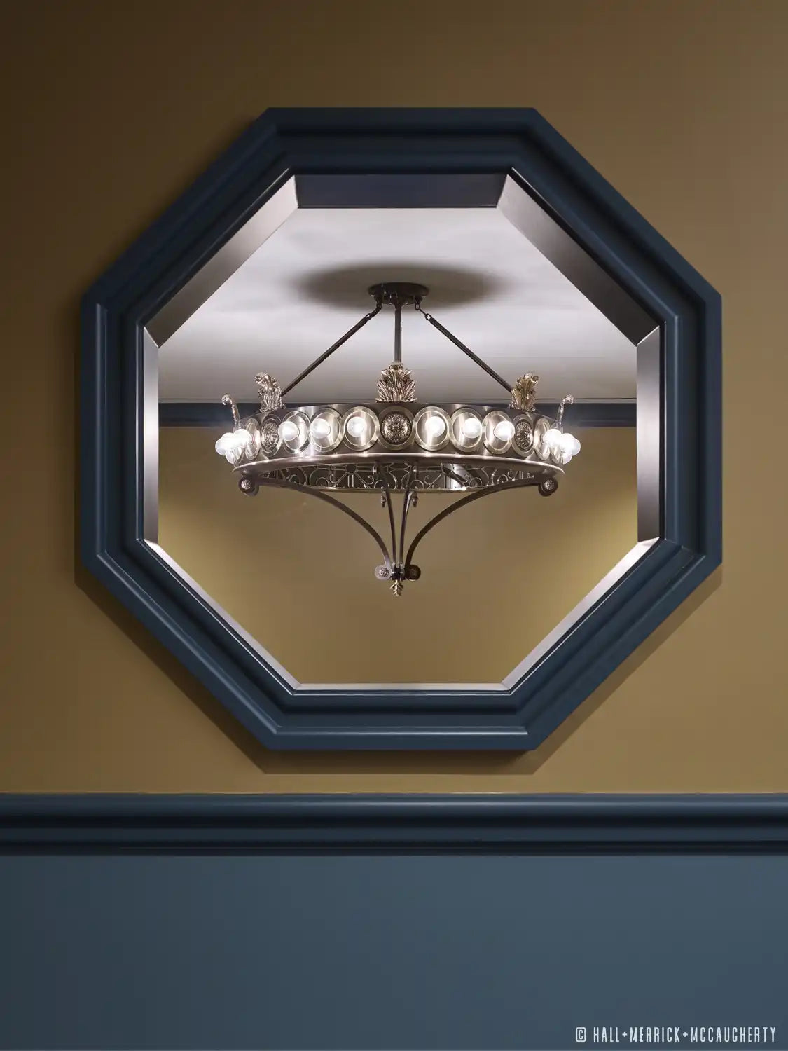 Ornate bronze chandelier with multiple glass bulbs, framed by an octagonal mirror.