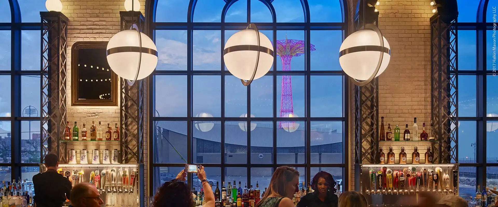 A lively bar with a view of a city skyline at dusk.