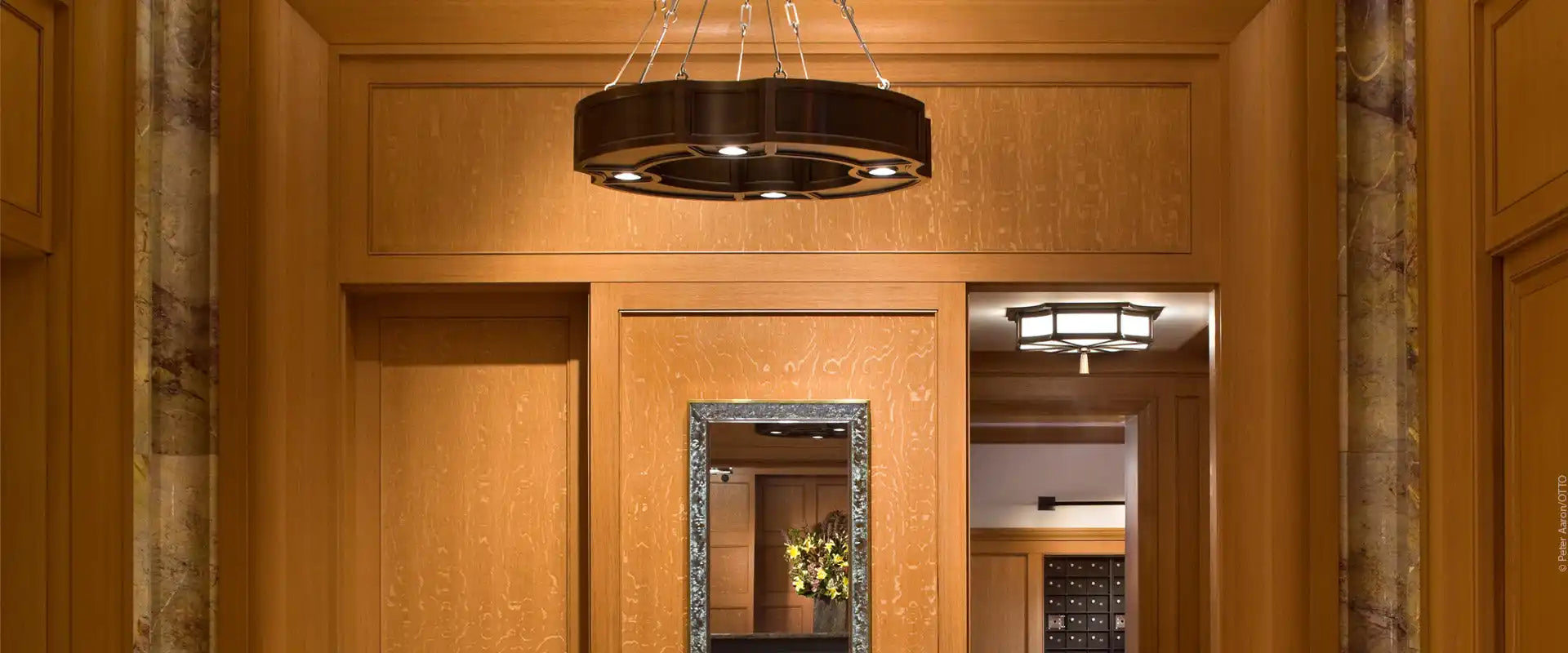A sophisticated wood-paneled lobby with a central mirror and modern light fixtures.